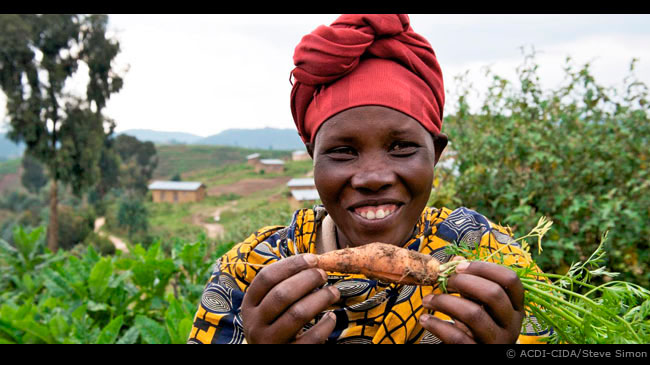 acdi Dans une région du Rwanda, une femme montre fièrement une carotte qu'elle a cultivée dans ses jardins après avoir participé à un project financé par l'ACDI